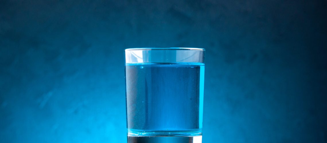 side-view-still-water-glass-wooden-cutting-board-blue-background
